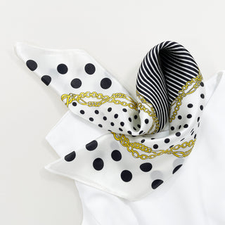 Square silk scarf with white background, black polka dots, black and white striped border, and decorative gold chain print pattern, elegantly folded