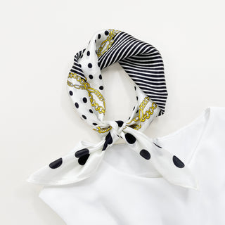 Square silk scarf tied with black polka dots, black stripes, and gold chain pattern on white background, showcasing versatile 53cm bandana design