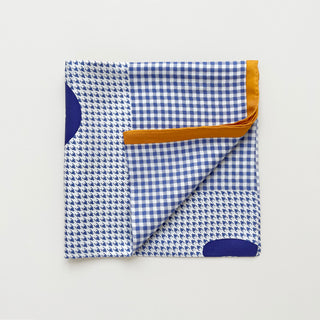Folded checkered and houndstooth silk twill scarf in purple and white with orange contrast border and hand-rolled edges.