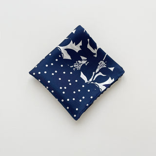 Folded navy blue silk square scarf with white floral and polka dot pattern on a light grey background