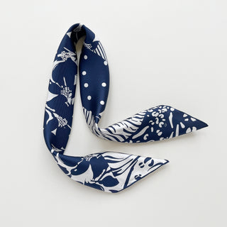 Navy blue and white patterned silk scarf featuring mixed floral, polka dot, and animal print motifs on a light grey board