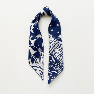 Navy blue and white patterned silk scarf featuring mixed floral, polka dot, and animal print motifs on a light grey background