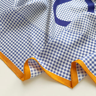 Close-up of houndstooth and checkered silk twill scarf in blue and white with orange contrast border and hand-rolled edges.