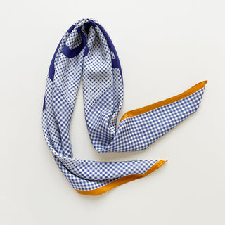 Blue and white checkered silk scarf with orange border on a light grey background