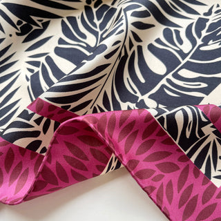 Luxury silk scarf featuring black tropical leaf pattern on light beige background with vibrant magenta border, double-side printed, showing elegant drape and hand-rolled edges