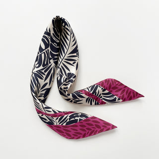 Women's silk scarf with black tropical leaf pattern on light beige background, featuring magenta leaf-printed border and hand-rolled edges, elegantly displayed