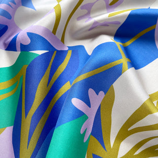 Close-up of a luxurious abstract lotus silk scarf in vibrant blue, teal, lilac, and mustard yellow patterns.