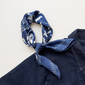 a rich blue silk scarf suits for both women and men featuring botanic leafy print knotted as a neckerchief, paired with a dark blue denim top