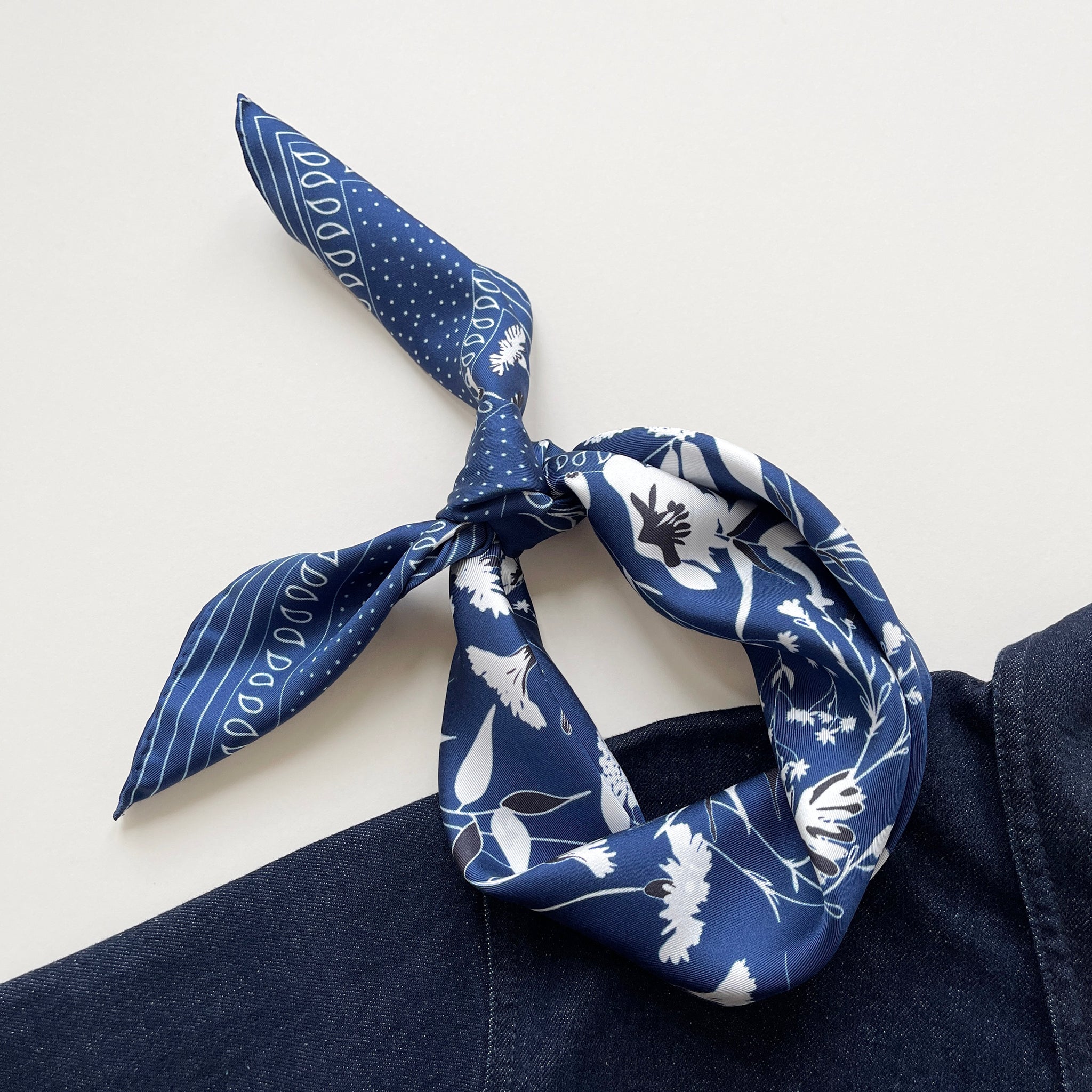 a rich blue silk scarf featuring botanic leafy print and hand-rolled hems knotted as a headband, paired with a dark blue denim top