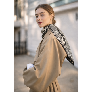 A woman wearing a beige trench coat and a black-and-white patterned 90cm silk scarf, photographed on a city street.