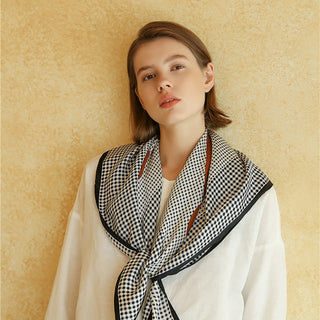 Woman wearing a black and white checkered silk scarf with black border, hand-rolled edges, against a beige background.
