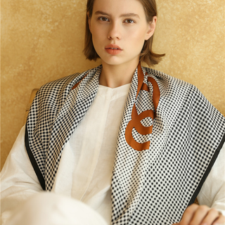 Woman wearing a black and white checkered silk scarf with black border, hand-rolled edges, against a beige background.