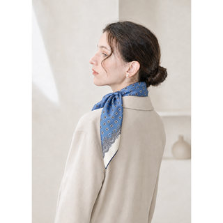 Woman wearing a cornflower blue vintage medallion 65cm silk square scarf tied at the back of her neck, styled with a low bun and ivory jacket.