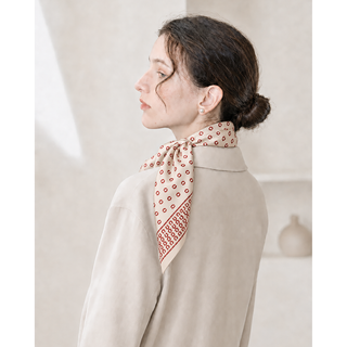Woman wearing a beige and red horseshoe print silk satin scarf tied at the neck with an elegant cream blouse.