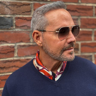 Man wearing a berry-purple, orange and cream Berry Blossom silk neckerchief tucked into a navy V-neck jumper.
