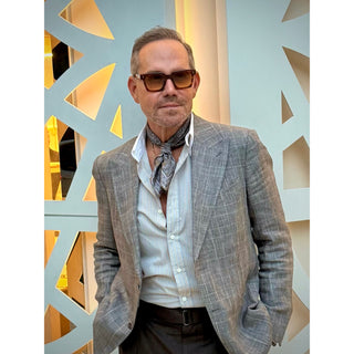 Man wearing a grey and taupe tone patterned silk square from LuluLane in a grey suit and sunglasses posing in front of decorative wall showcasing a polished smart casual look.