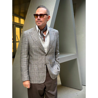 Man wearing a grey and taupe tone patterned silk square scarf from LuluLane in a grey suit and sunglasses showcasing a polished smart casual look.