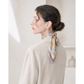 Woman wearing a lilac peony print silk neck scarf tied neatly at the back of the neck, styled with a cream coat and pearl earrings.
