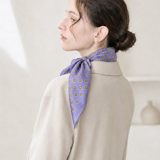 Woman wearing a lavender purple mini floral silk scarf tied elegantly at the back of the neck, styled with a low bun in soft natural light.