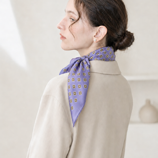 Woman wearing a lavender purple mini floral silk scarf tied elegantly at the back of the neck, styled with a low bun in soft natural light.