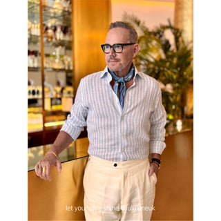 Men’s silk and cotton neck scarf in light blue with stylised bird print, styled with a white and blue striped shirt, cream white trousers.