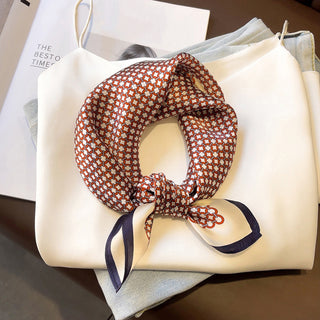 Red and navy lattice pattern silk bandana scarf with navy border, tied elegantly on cream handbag with soft fabric background