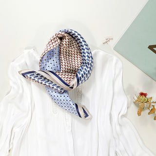 Blue geometric silk bandana with mixed patterns of zigzags and dots in blue, cream, and brown tones, styled on a white blouse