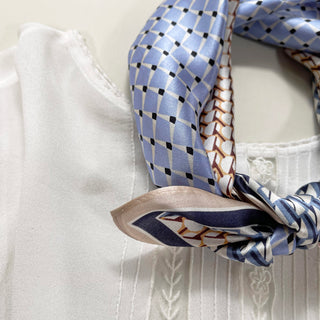 Luxurious blue silk bandana with geometric checkered pattern, featuring black accents and tan border, elegantly knotted on white fabric