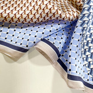 Luxurious silk scarf featuring blue geometric patterns with black accents, beige border, and complementary tan geometric design, showcasing its silky texture and versatile style.
