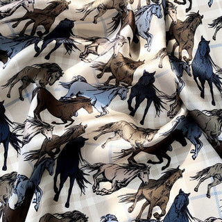 Luxury silk scarf with galloping wild horses pattern in brown, blue, and black on cream background, showing the fabric's soft texture and drape.