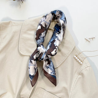 Elegant silk horse print bandana scarf with brown and blue equestrian motif, styled on a beige jacket with pearl accessories