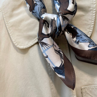 Luxurious silk bandana scarf with brown and blue wild horse pattern, tied elegantly against cream fabric, displaying shimmering texture