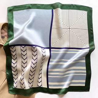 Square silk scarf with green border and geometric pattern featuring light blue sections, navy chevron details, and concentric squares in cream and blue tones