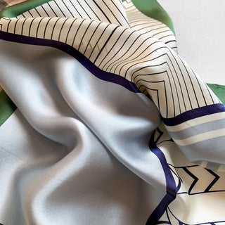 Silk bandana with modern geometric pattern featuring cream background, purple borders, and linear designs, showing luxurious sheen of premium silk fabric