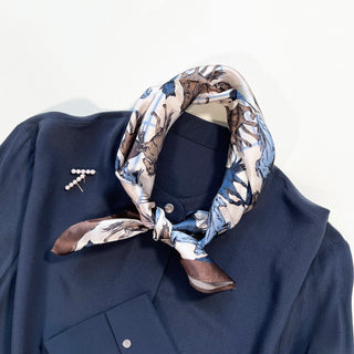 Silk horse print bandana scarf in cream, blue and brown tones, styled on navy blouse with pearl pin, showcasing elegant equestrian design