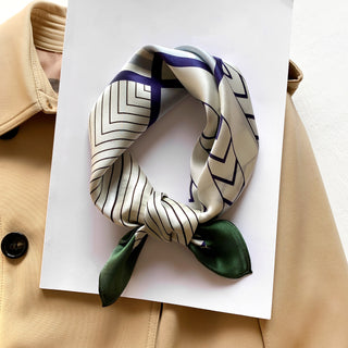 Silk bandana with modern geometric pattern in ivory, navy and green, elegantly tied and displayed on white paper against beige coat