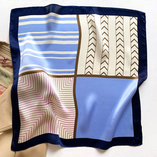 Square silk scarf with navy border featuring geometric pattern blocks in blue, cream, and pink with chevron and stripe designs