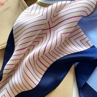 Luxury silk scarf featuring pink geometric lines on cream background with navy blue border, showing the fabric's soft sheen and texture