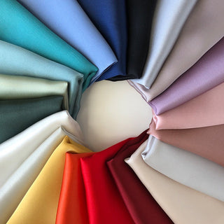 Premium silk scarves arranged in a circular pattern showcasing multiple colors including burgundy, navy blue, sky blue, teal, red, yellow, and pastel shades with a lustrous finish.