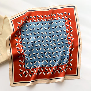Square silk bandana with dancing hat pattern in blue center, red border, and cream edge, elegantly displayed showing its shimmering texture.