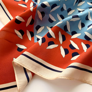 Luxurious silk bandana featuring red and blue panels with white hat pattern design, bordered by navy and cream trim, showcasing the scarf's silky texture