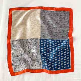 Square silk neckerchief with patchwork design featuring cream paisley, blue with white paisley pattern, and gray textures, bordered in bright orange