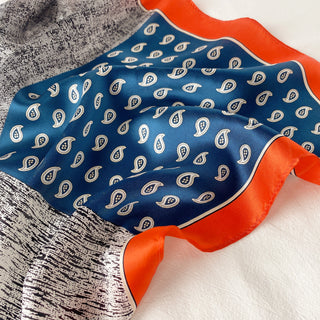 Luxurious 100% silk neckerchief featuring blue center with white paisley pattern, vibrant orange border, and patchwork design elements