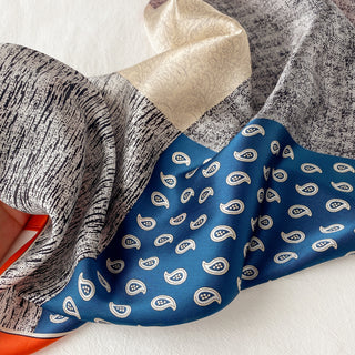 Silk paisley patchwork neckerchief featuring blue with white paisley pattern, cream sections, and textured gray areas, displaying the luxurious sheen of 100% silk.
