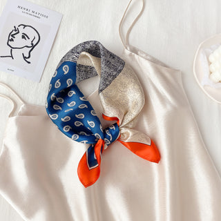Paisley patchwork silk neckerchief with blue, cream, and orange sections, styled on cream fabric with Matisse artwork visible