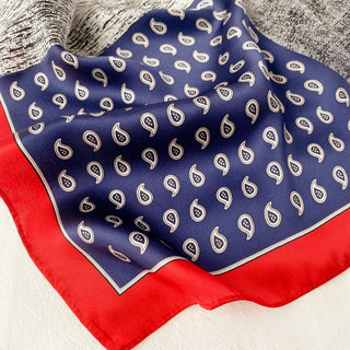 Navy blue silk neckerchief with white paisley pattern and bright red border, displaying luxurious sheen and delicate draping of 100% silk fabric