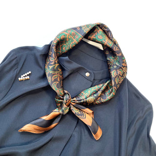 Elegant black and green paisley silk neckerchief tied around collar of navy shirt, featuring intricate floral patterns and gold accents