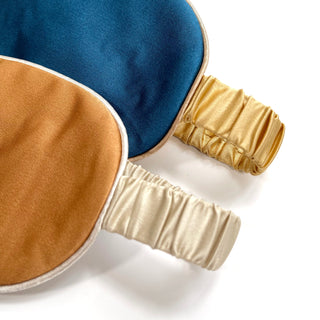 Luxury double-sided silk sleep mask featuring deep blue and caramel colors with elegant gold and cream elastic bands for comfort