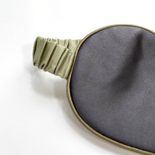 Double-sided silk sleep mask featuring gray fabric on one side and light sage green elastic band, showcasing luxury texture and elegant design.