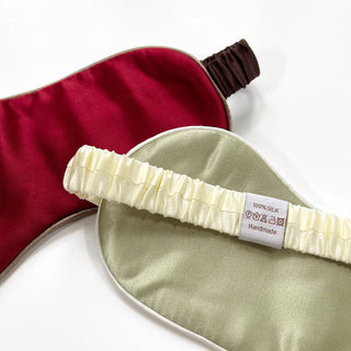 Double-sided luxury silk sleep mask featuring rich burgundy red and caramel gold sides with elastic bands and 100% silk handmade label